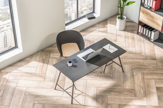 Top side view on stylish dark work table with laptop on wooden parquet floor in spacious sunlit home office with city view from big windows. 3D rendering