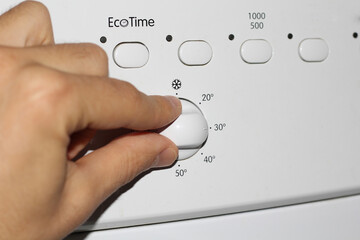 Man's hand presses the buttons on the control panel of the washing machine