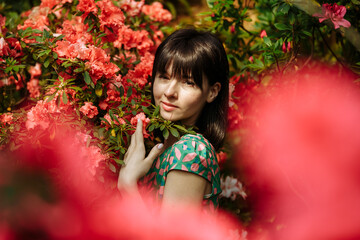 Naklejka premium Beautiful brunette in a garden of azaleas in a green dress
