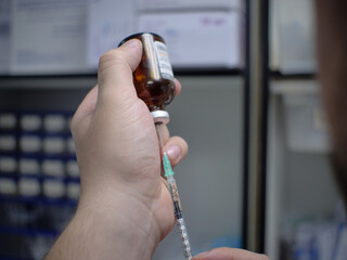 The doctor holds a bottle of medicine in his hand and with the other hand draws a solution from it with a syringe. Close-up. The doctor will draw up a medicine to give an injection to a sick patient.