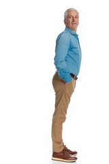 Naklejka premium old man with grey hair holding hands in pockets and looking behind