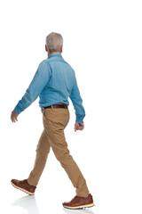 Naklejka premium side view of casual old man with sneakers looking away and walking