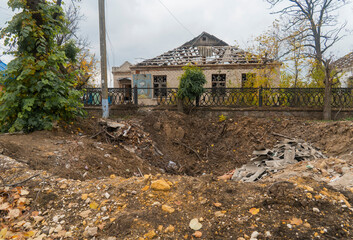 Crater in the ground from a bomb explosion against the background of a house destroyed by shelling....