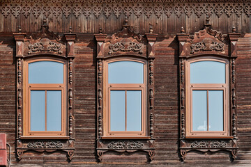 Three windows with carved wooden architraves. Facade of old wooden merchant house. Siberia, Russia.