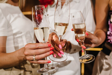 Young bridesmaids clinking with glasses of champagne in hotel room. Closeup photo of cheerful girls celebrating a bachelorette party. Females have toast with wine. Celebration. Bachelorette party.