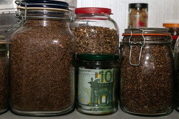 Euro banknotes in a glass jar among other jars with cereals and dried fruits. Keeping money in a glass jar. Financial reserve. Keeping cash at home. Money saving concept. Secret piggy bank.