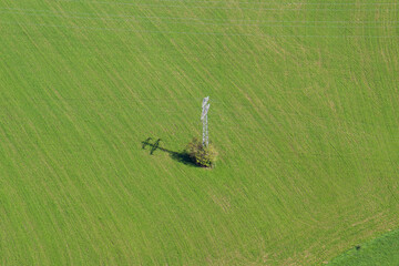 A electricity power line pylon from above on a green farm land