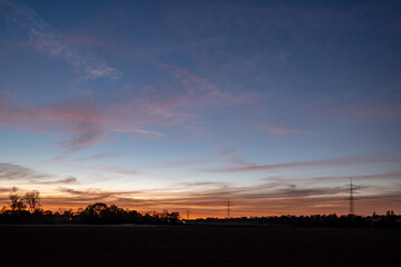 Beautiful dramatic orange and blue cloud and sky after storm and raining over agricultural field and high voltage tower on countryside in Germany. Nimbostratus cloud during sunset. 