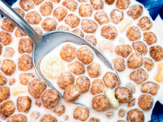 Metal spoon in a plate with milk and corn balls close-up. Healthy balanced breakfast of corn flakes and milk. Flat layout. View from above.
