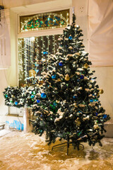 Christmas tree decorated with lights illuminating and balls bauble and New Year's garlands on outside. Xmas tree in front of building on street