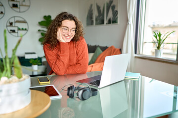 Young smiling pretty woman student using laptop elearning or remote working at home office looking...