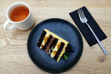 creative food design concept, top view, dark blue plate, cup of tea, fork, cake.