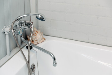 Bathroom with a shiny faucet, shower, white bathtub and a shell in the corner