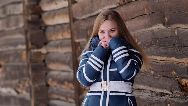 A young schoolgirl poses in winter in the countryside against the backdrop of a barn.