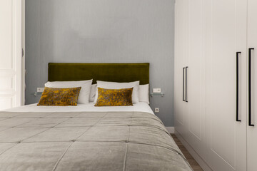 Detail of a Bedroom with white cabinet doors, bed with ocher green cushions and gray bedding