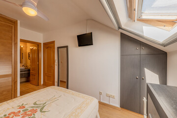 Classic style bedroom with fitted wardrobe with Venetian style wooden doors with sloping ceilings and skylight