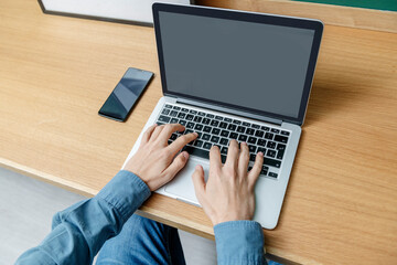 Man's hands on the keyboard of a laptop on top of a wooden table