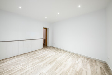 Empty room with wood-like stoneware floor, plain white walls and lamps on the plaster false ceiling