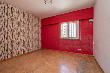 Empty room with oak parquet floor, red painted walls and another wallpaper with branch motifs