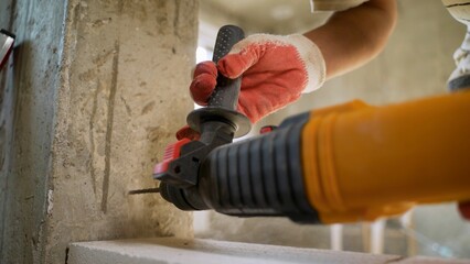 The master drills a wall for fixing the future foam block. A builder with a pneumatic hammer drills...