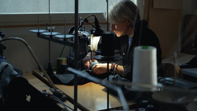 A female tailor seamstress repair old jeans with vintage darning machine in a workshop repairing denim clothes. Small family business, tailoring and repair of clothes, handmade, startup.