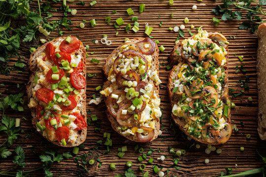 Sandwiches with scrambled eggs and various vegetables, sprinkled with fresh herbs on a wooden table, top view