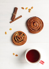 Sweet buns with raisins and cinnamon, a cup with a hot drink and autumn leaves. On a light wooden background,flatlay