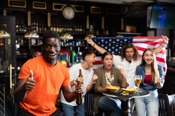 Happy excited african american man watching baseball in sports bar, giving thumbs up approving good...