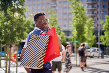 Smiling young african american man carrying shopping bags and looking at camera