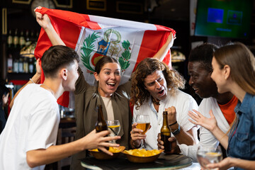 Cheerful multiracial football fans waving the flag of England while drinking beer and watching tournament in sport bar