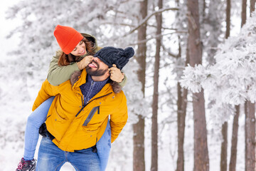 Fototapeta na wymiar Boyfriend piggybacking girlfriend on snowy winter day