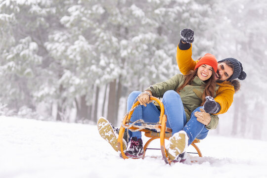 Couple sitting on sled and sliding down the hill while on winter vacation
