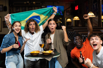 Fototapeta Emotional cheerful young adults friends, football fans cheering for favorite Brazil team together while watching match on tv in sports bar obraz