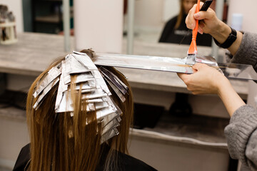 Hairdresser is dyeing female hair, making hair highlights to his client with a foil.