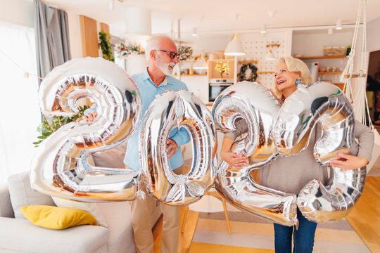 Senior couple holding balloons 2023 while celebrating New Year at home