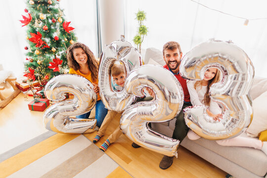 Family holding giant balloons shaped as numbers 2023 representing the upcoming New Year