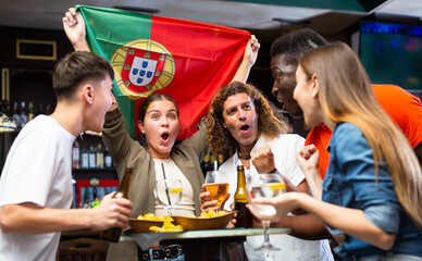 Group of Portugal football team fans spending time in bar, drinking bear and having fun. People with state flag in pub.