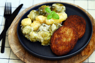 Schnitzels with potatoes and Brussels sprouts in white sauce. A dish of German cuisine.