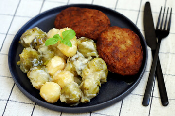 Schnitzels with potatoes and Brussels sprouts in white sauce. A dish of German cuisine.