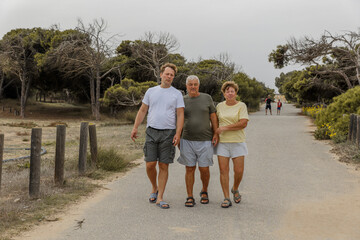 Elderly parents with an adult son walk in the park, communication and care for loved ones