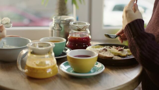female hands having breakfast cafe table teapot fruit tea cake bowl on wooden table. autumn winter cold weather warm atmospheric cafe meal. tasty food indoors eat out concept. wine colors yellow red