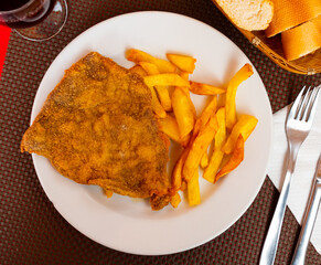 Appetizing crunchy breaded beef cutlet served with fried potato on white plate