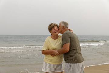 Happy senior couple walking on the beach in a sunny day. Smiling mature couple looking at each other on beach with copy space. Retired man in love with his wife relaxing during vacation.