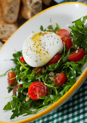 Colorful salad with Italian cow milk cheese burrata on pillow of fresh rocket with cherry tomatoes..