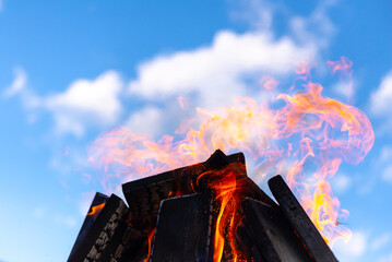 A large fire made of planks. Firewood in a bright flame. Bonfire against the blue sky