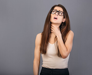 Suffering business woman holding the throat with pain and unhaapy face in eyeglasses looking up on grey copy space background. Waiting the sick leave in office work. Closeup