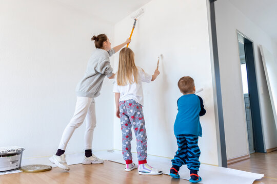 Young adult single happy woman with two children daughter an son painting wall paint roller brush white color living room moving new home flat . Female painter diy interior renovation apartment home