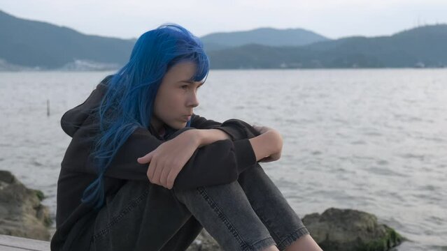 Girl with blue dyed by sea. A pensive teen with dyed hair style think about her life by the calm sea in summer.
