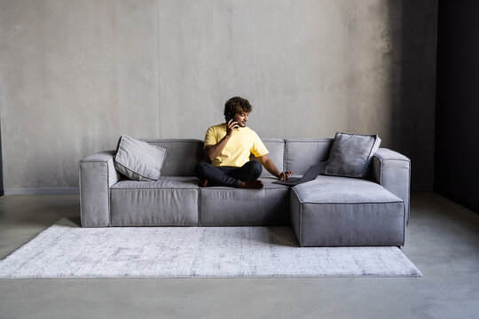 Happy man relaxing on couch while video calling using laptop at home. Latin man sitting on sofa and making a video call. Smiling middle eastern businessman doing online video.