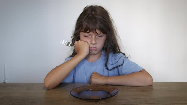 Poor child with empty plate in kitchen. A poor little girl wait for meal in the empty kitchen. A concept of poverty and hungry time in the world.
